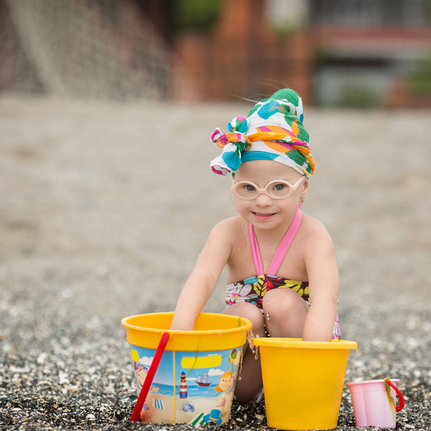piękna dziewczyna z zespołem Downa, grając z piasku na plaży - Zdjęcie, obraz