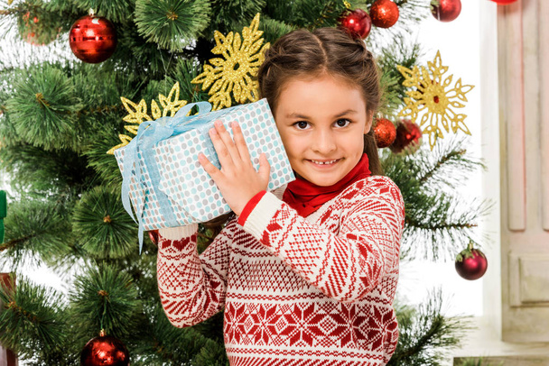 uśmiechający się małe dziecko trzyma prezent na Boże Narodzenie przed choinki - Zdjęcie, obraz