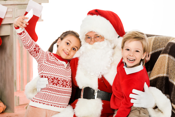 Kinder machen Selfie mit Weihnachtsmann, während sie zusammen im Sessel sitzen - Foto, Bild