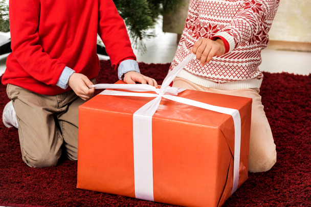 обрезанный снимок детей, открывающих подарок на Красное Рождество
 - Фото, изображение