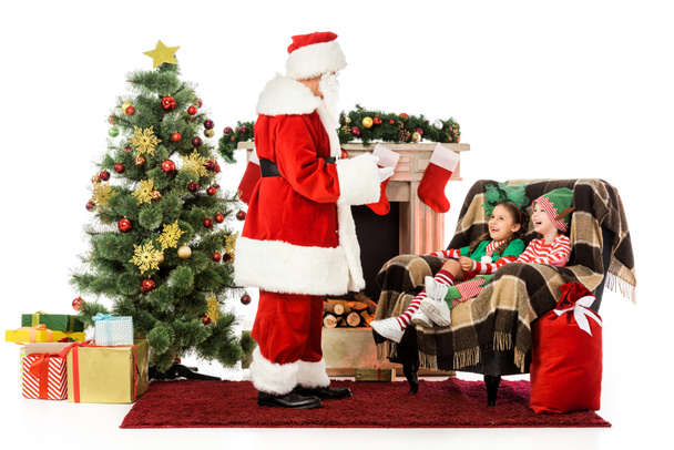 Santa praten met kinderen terwijl zij zittend in zijn leunstoel geïsoleerd op wit - Foto, afbeelding