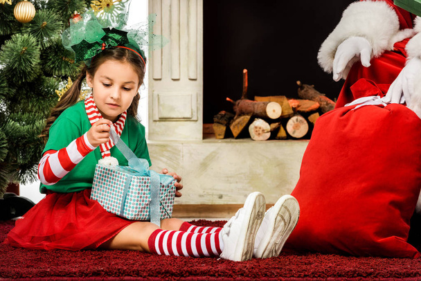adorable little child sitting on carpet with christmas gift near santa - Фото, изображение