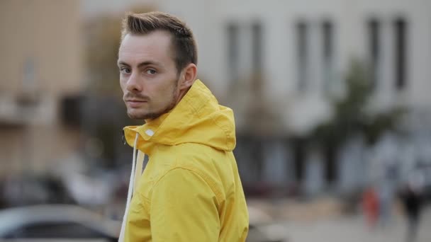 Portrait of young caucasian confident man wear hood of yellow windbreaker in city - Video, Çekim