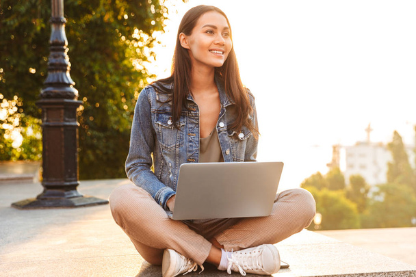 Pretty young asian girl using laptop while sitting on a city street - Foto, Imagen