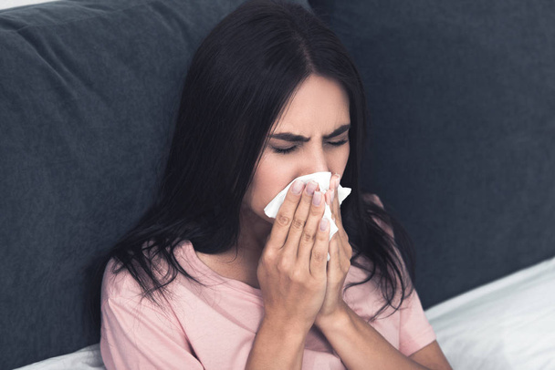 diseased young woman with box of paper napkins sneezing while sitting in bed - Foto, Imagem