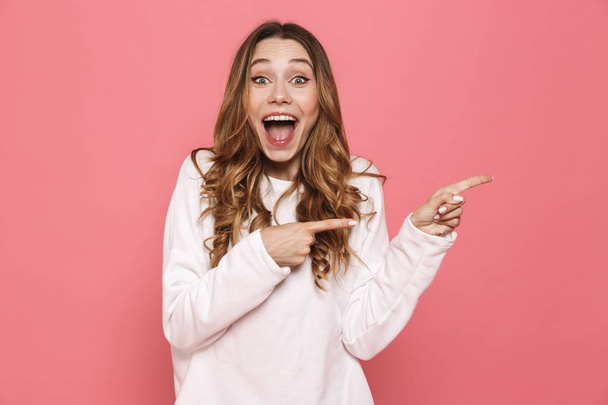 Portrait of an excited young casual girl pointing at copy space isolated over pink background - Valokuva, kuva