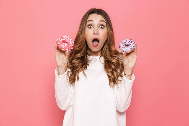 Portrait of a surprised young woman showing donuts isolated over pink background - Fotografie, Obrázek