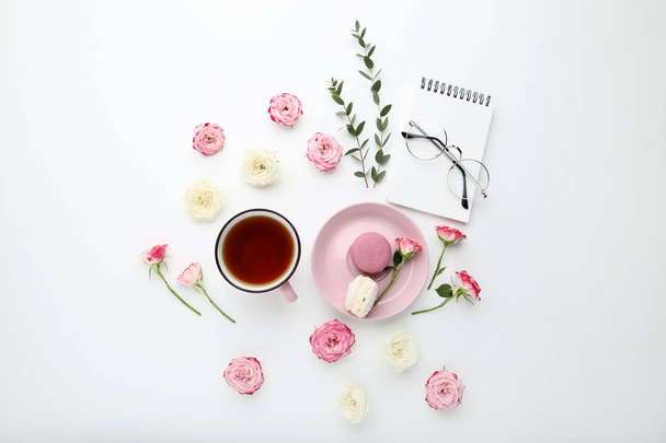 Flores de rosas con taza de té y macarrones sobre fondo blanco
 - Foto, imagen
