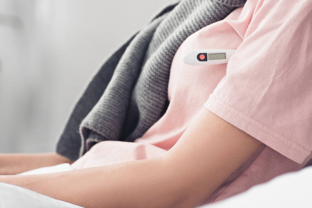 обрізаний знімок жінки, що вимірює температуру з електронним термометром у ліжку
 - Фото, зображення