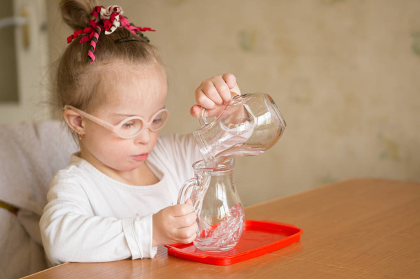 Mädchen mit Down-Syndrom gießt sanft Wasser aus einem Krug in einen Krug - Foto, Bild