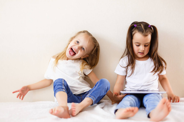 Dwie małe dziewczynki, zabawy siedzi na łóżku za pomocą cyfrowego tabletu - Zdjęcie, obraz