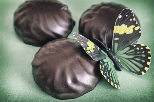 Em um fundo verde marshmallow cheio de chocolate. Próximo decoração na forma de uma borboleta artificial
. - Foto, Imagem