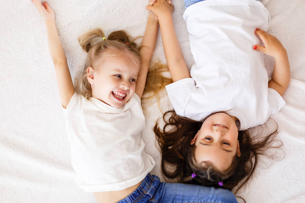 two happy little sisters lying on white bed, top view - Fotografie, Obrázek