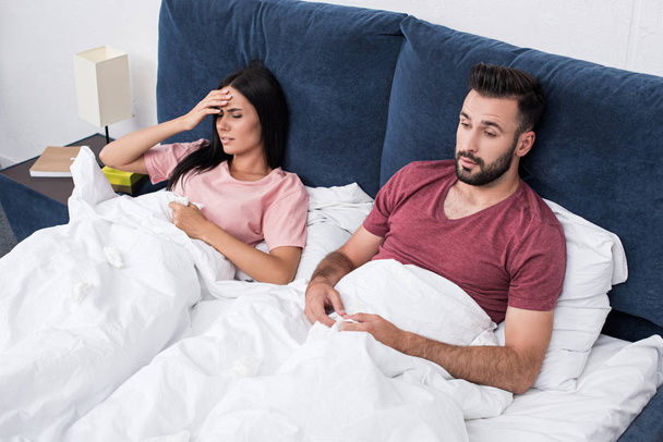 high angle view of young sick couple sitting in bed - Photo, Image