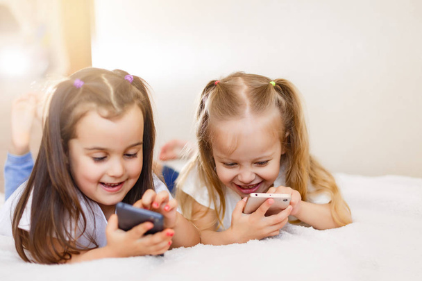 Happy μικρά κορίτσια με τα smartphones που βρίσκεται στον όροφο στο σπίτι - Φωτογραφία, εικόνα