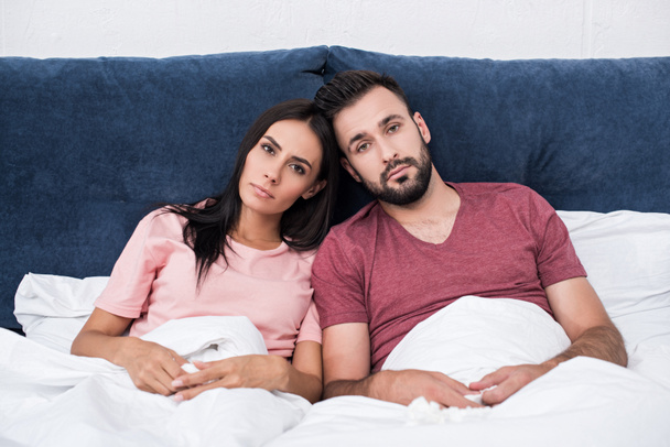 unemotional young couple leaning at each other while sitting in bed and looking at camera - Фото, зображення