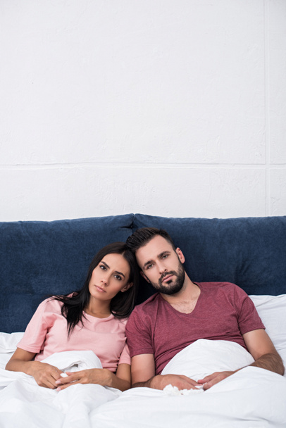 serious young couple leaning at each other while sitting in bed and looking at camera - Foto, Imagem