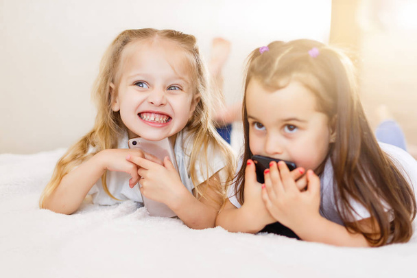 happy little girls with smartphones lying on floor at home - Foto, afbeelding