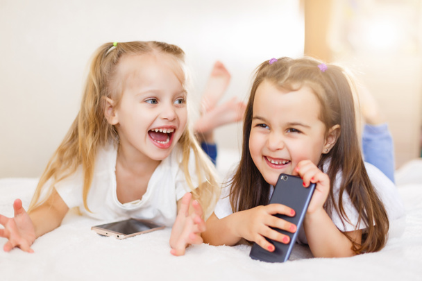 glückliche kleine Mädchen mit Smartphones, die zu Hause auf dem Boden liegen - Foto, Bild
