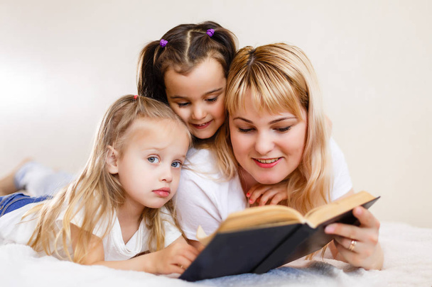 concepto familiar amoroso feliz. bonita joven madre leyendo libro a sus pequeñas hijas acostadas en la cama
 - Foto, imagen