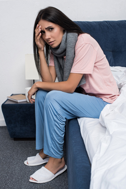 sick young woman in scarf suffering from headache while sitting on bed - Fotografie, Obrázek