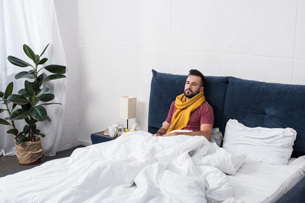 depressed sick young man lying in bed in scarf and looking away - Foto, Imagem