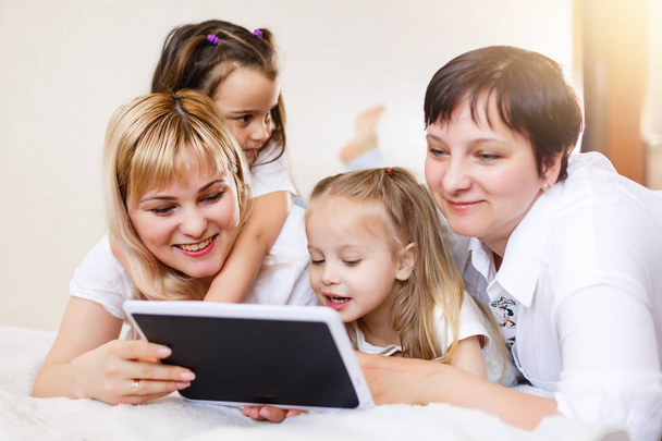 happy mothers and their daughters using digital tablet lying on sofa - Foto, Imagen