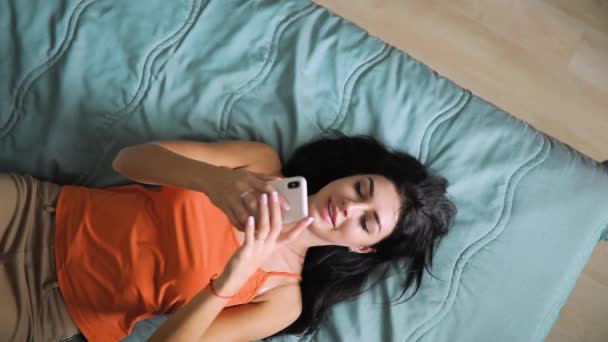 Woman write message by cell phone lying on bed, top view - Filmati, video