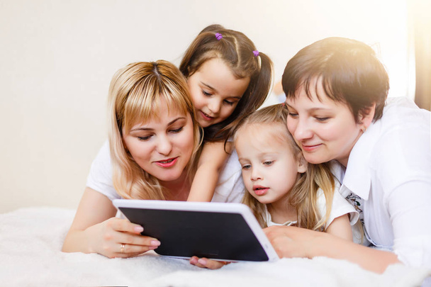 happy mothers and their daughters using digital tablet lying on sofa - Foto, Imagem