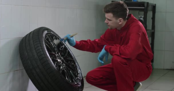 Pracownik myjni samochodowej jest mycie kół z pędzla starannie slowmotion - Materiał filmowy, wideo