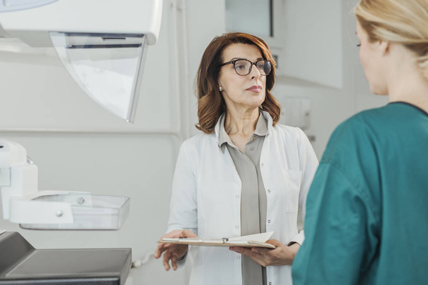 Pretty Caucasian woman doctor talking with her patient on breast examination. - Zdjęcie, obraz
