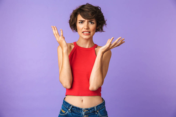 Portrait of a frustrated young girl shrugging shoulders isolated violet background - 写真・画像
