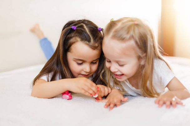 Дві маленькі дівчата малюють свої нігті, лежачи на ліжку вдома
. - Фото, зображення