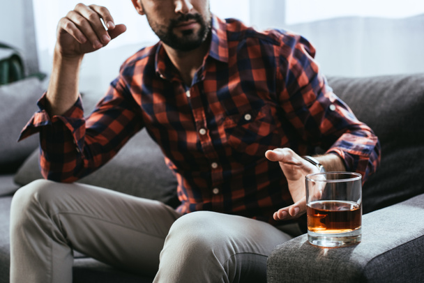 Schnappschuss eines jungen Mannes, der ein Glas Whiskey nimmt, während er auf der Couch sitzt - Foto, Bild
