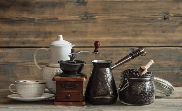 Roasted coffee beans in glass jar, coffee grinder and jezva on wood table - Fotoğraf, Görsel