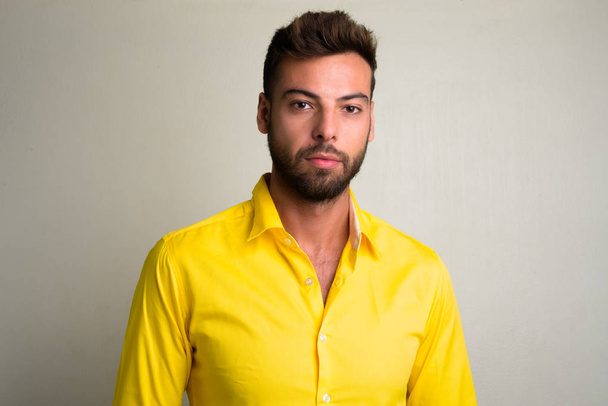 Studio shot of young handsome bearded businessman wearing yellow shirt - Foto, imagen
