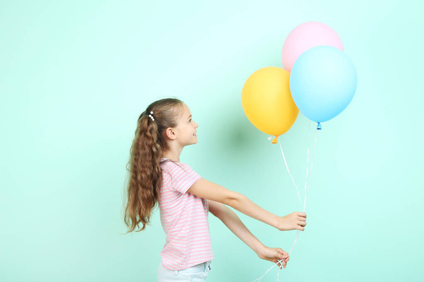 Cute young girl with colored balloons on mint background - 写真・画像