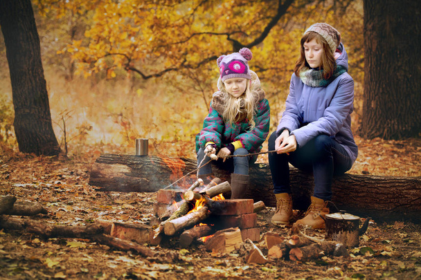 Two girls on picnic in the autumn forest sitting around the campfir - Fotó, kép