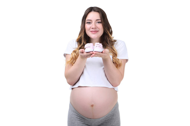 Pregnant woman holding baby shoes on white background - Foto, Imagen