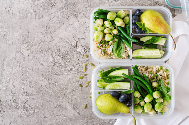 Contenants végétaliens de préparation de repas verts avec riz, haricots verts, choux de Bruxelles, concombre et fruits sur fond gris pierre
 - Photo, image