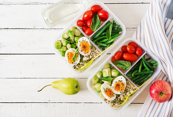 Вегетарианская еда готовит контейнеры с яйцами, брюссельской капустой, зелеными бобами и помидорами на белом деревянном фоне
 - Фото, изображение