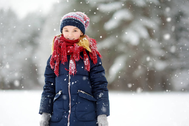 Adorable little girl having fun in beautiful winter park. Cute child playing in a snow. Winter activities for kid. - Fotó, kép