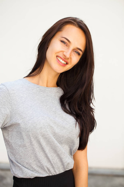 Glücklich Schöne brünette Frau in grauem T-Shirt, isoliert auf weißem Wandhintergrund - Foto, Bild
