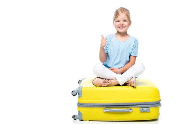 child sitting on yellow baggage and showing thumb up isolated on white - Φωτογραφία, εικόνα