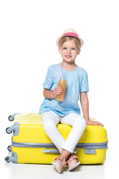 niño con bebida sentado en una bolsa de viaje amarilla aislada en blanco
 - Foto, Imagen