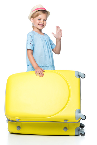 happy child waving and standing with yellow travel bag isolated on white - Photo, Image