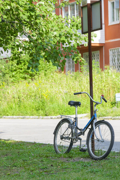 a black blue bicycle stands at a pillar on a summer day - Foto, imagen