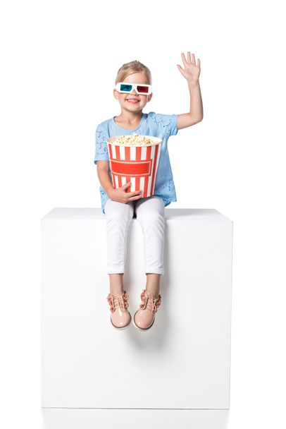 kind met popcorn zittend op witte kubus geïsoleerd op wit - Foto, afbeelding