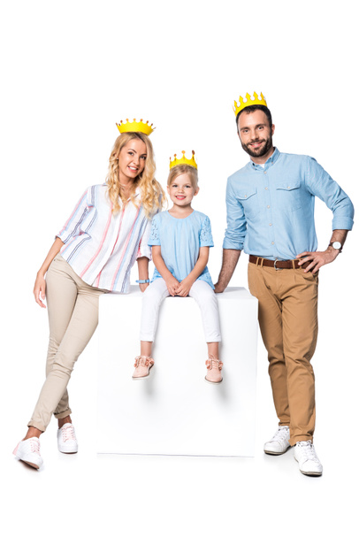 happy family with cardboard crowns sitting on white cube isolated on white - Photo, Image