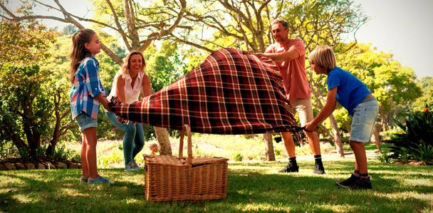 Family spreading the picnic blanket in park - Foto, imagen